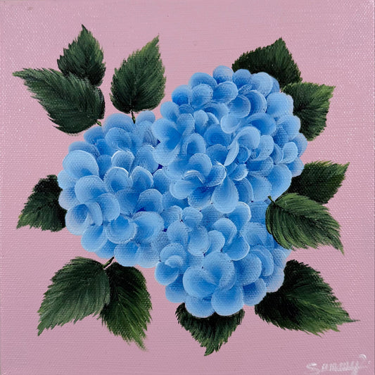 A square canvas painting featuring two blue hydrangea blooms with dark green leaves on a light pink background, mounted on a textured beige wall.