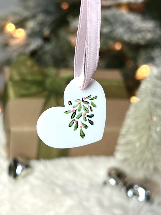 white acrylic heart ornament with hand painted mistletoe and a pink ribbon