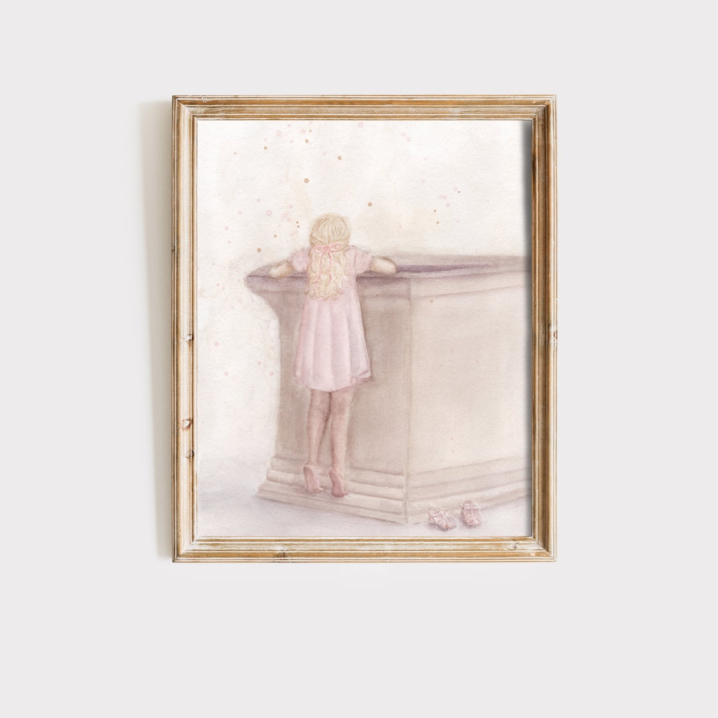 A framed art print featuring a watercolor-style illustration of a young girl in a pink dress leaning on a stone structure, set against a light off-white background.