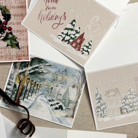 Collection of Christmas cards with winter scenes and festive text on a textured surface.