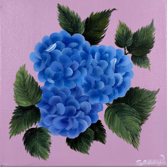 A square canvas painting featuring a vibrant blue hydrangea with dark green leaves on a light pink background, mounted on a textured beige wall.