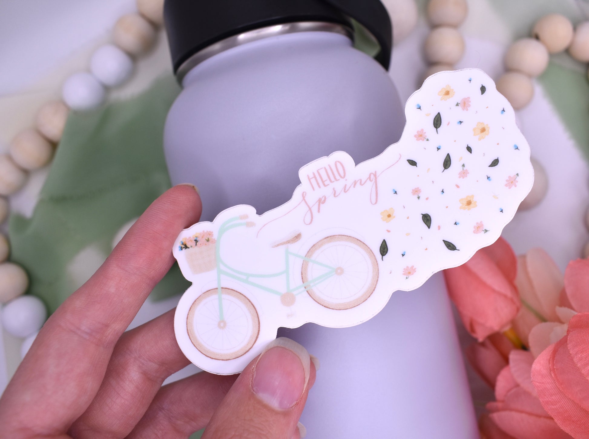 Spring sticker with a bicycle and flowers and the words "hello Spring" held over a water bottle